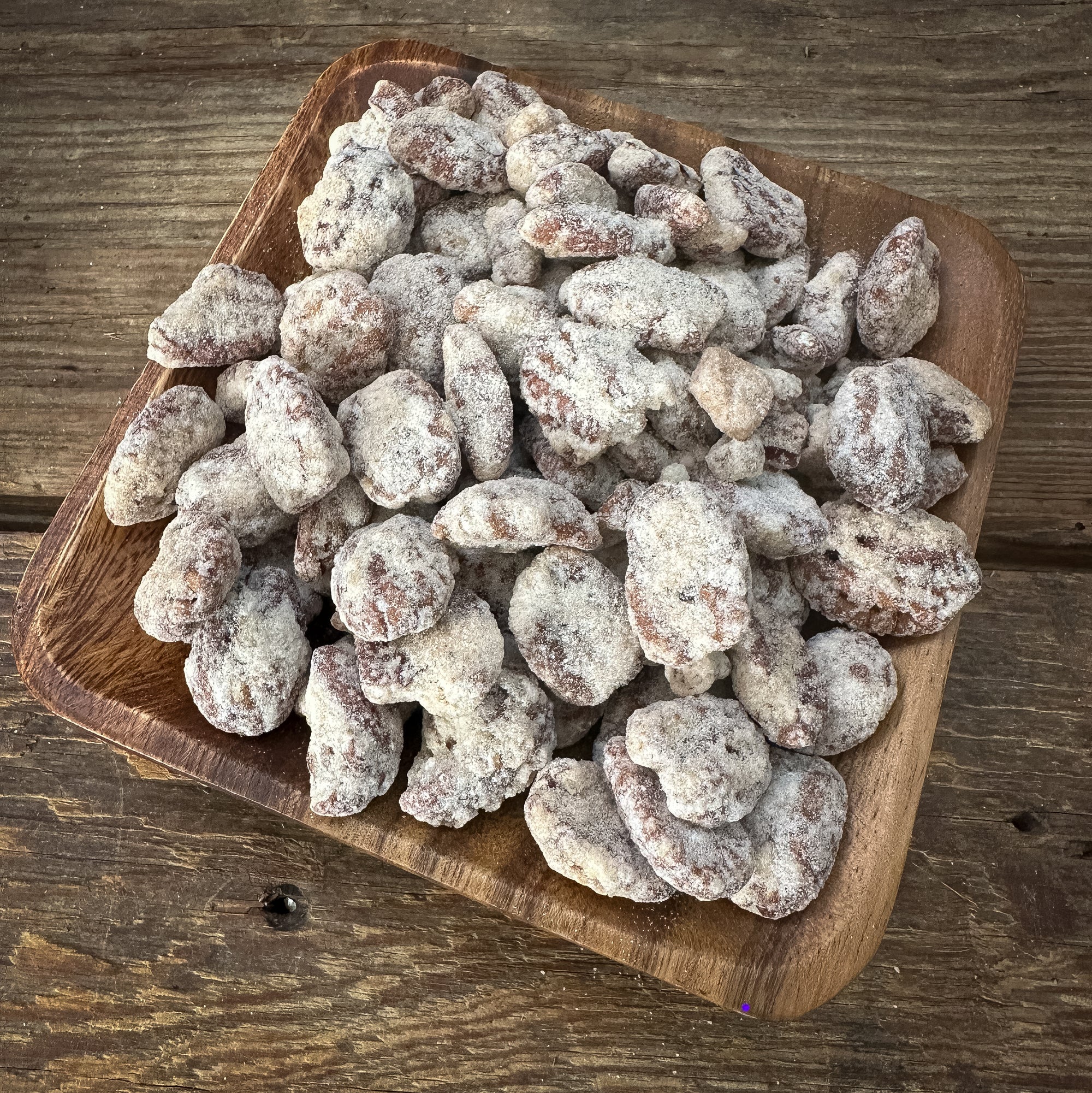 Wooden bowl filled with sugared almonds on a wooden surface