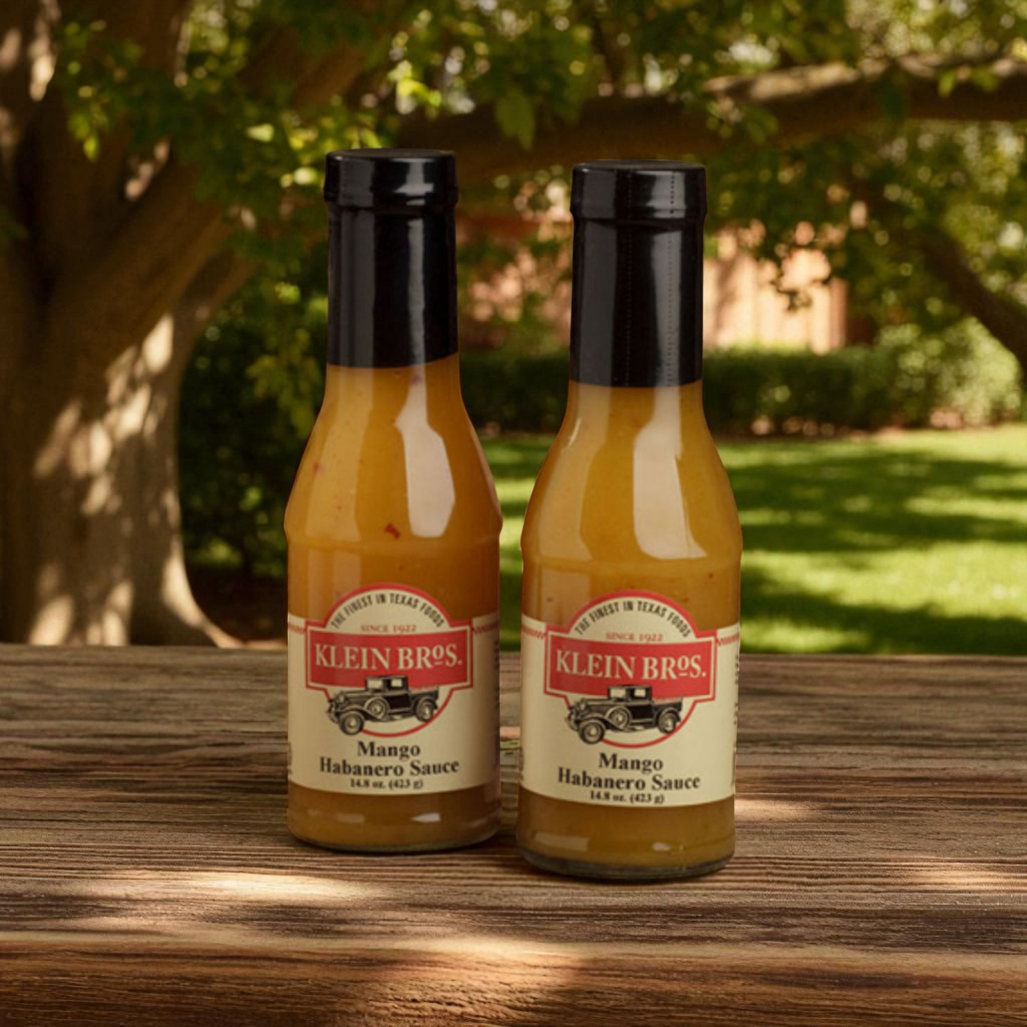 Two bottles of Klein Bros Mango Habanero Sauce on a wooden surface with a natural background.