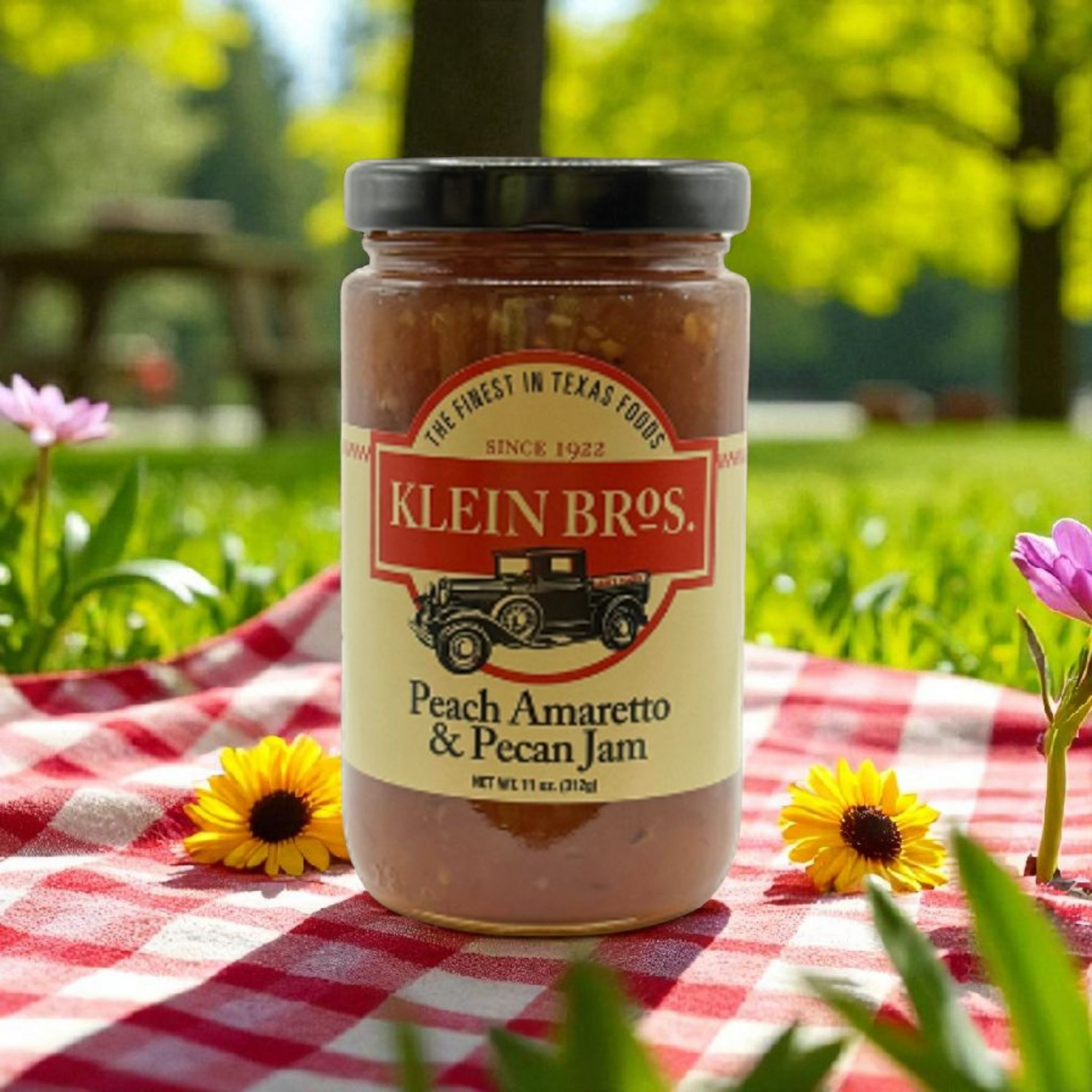 Jar of Klein Bros. Peach Amaretto & Pecan Jam on a red and white checkered tablecloth with flowers and greenery in the background.