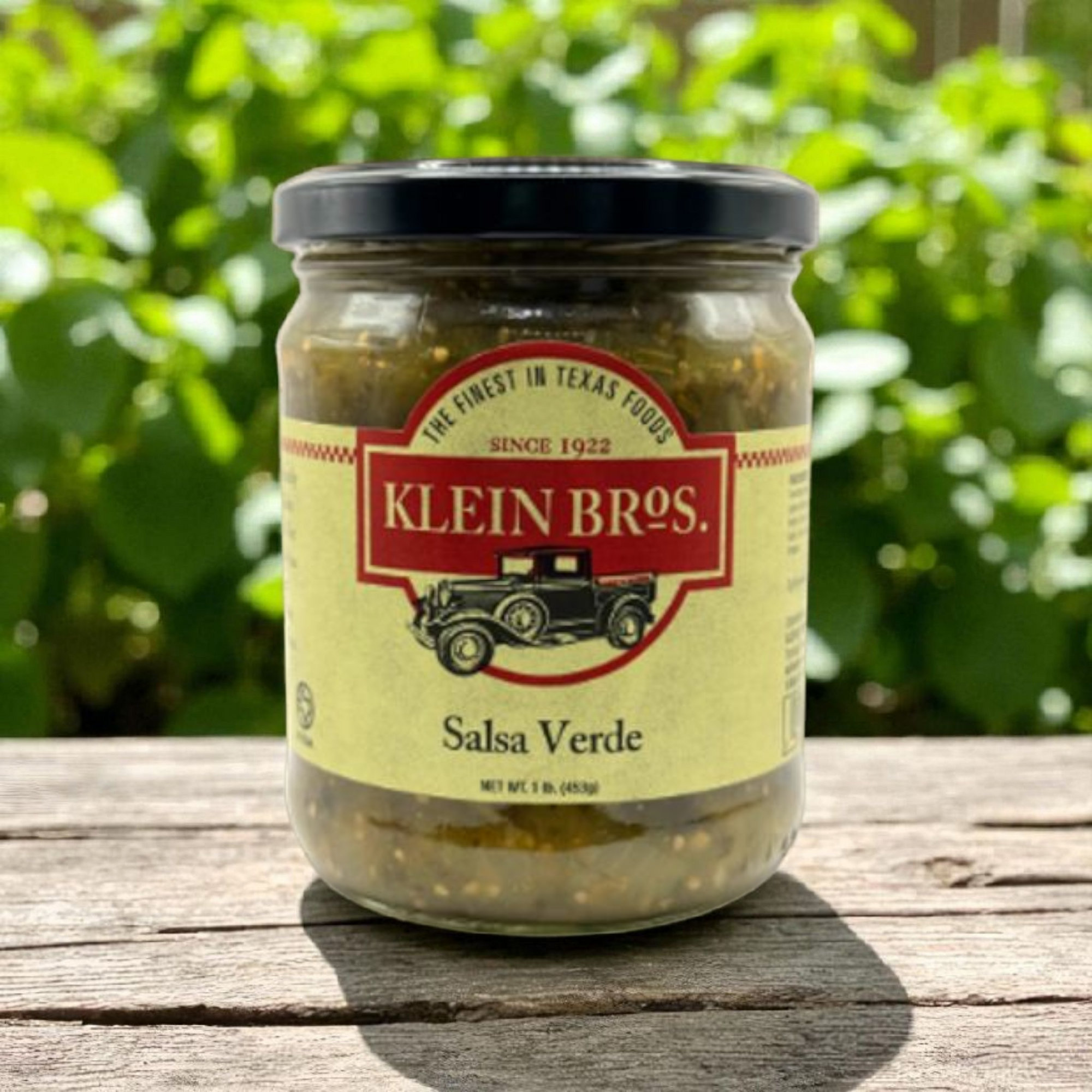 Jar of Klein Bros Salsa Verde on a wooden surface with greenery in the background