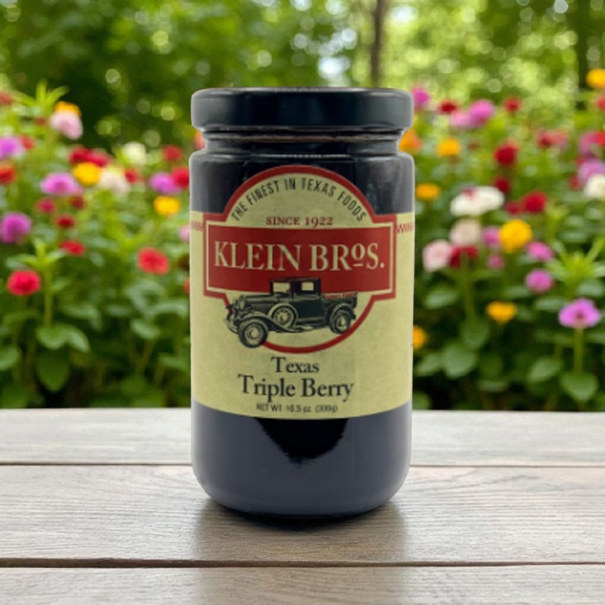Jar of Klein Bros. Texas Triple Berry on a wooden surface with flowers in the background
