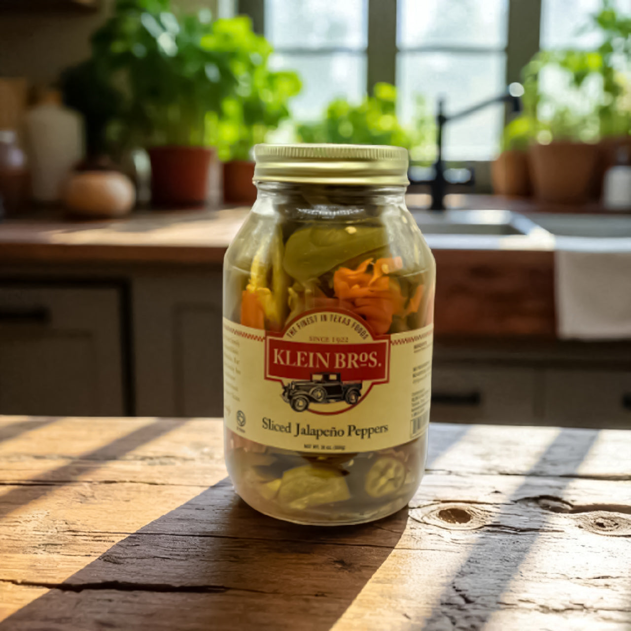 A jar of Klein Bros Sliced Jalapeño Peppers with carrots and olive oil, displayed on a rustic wooden kitchen counter in natural Texas sunlight.