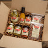 Box of Glen Bros food products including pickles, sauces, and nuts on a wooden surface.