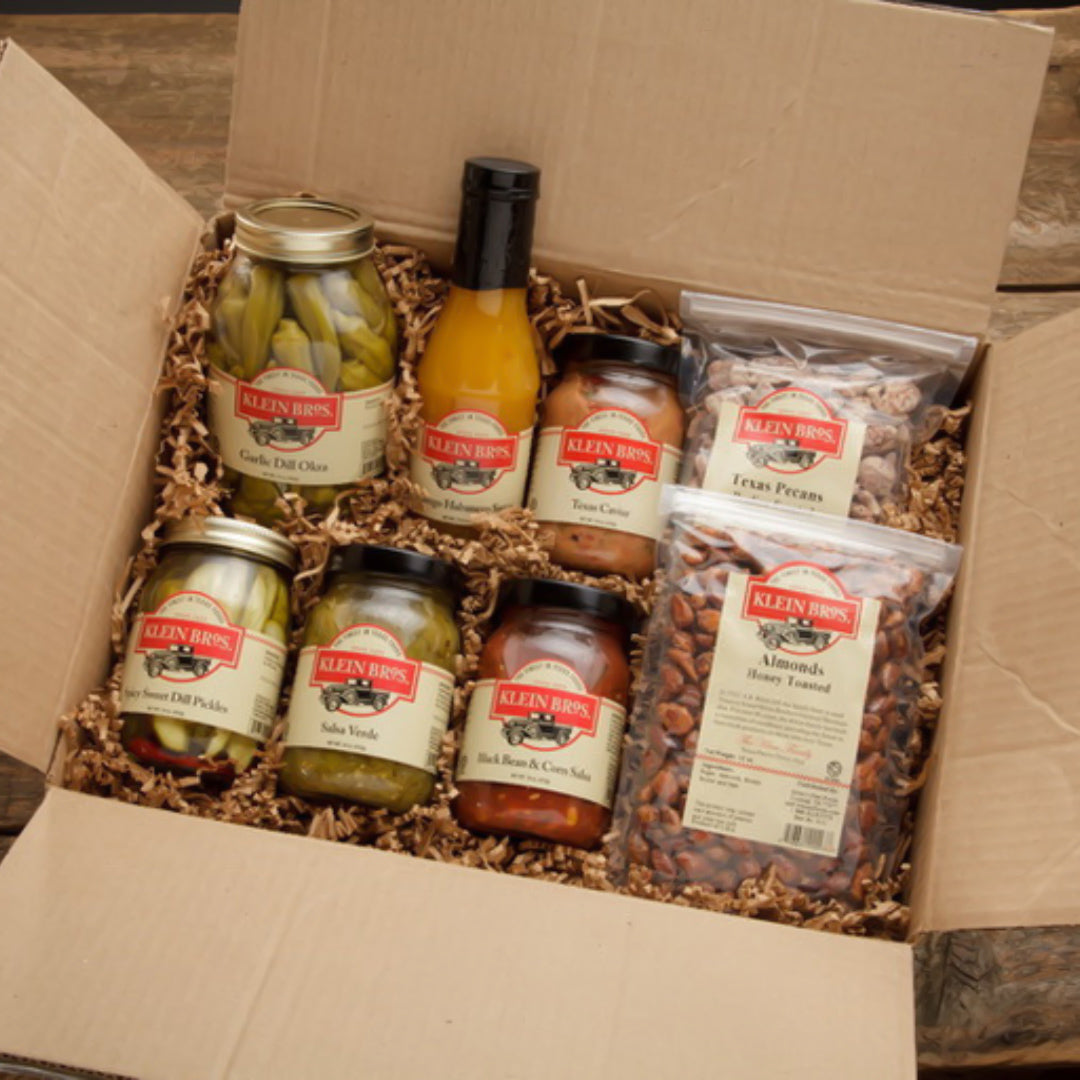 Box of Klein Bros brand food products, including jars and a bag on a wooden surface.