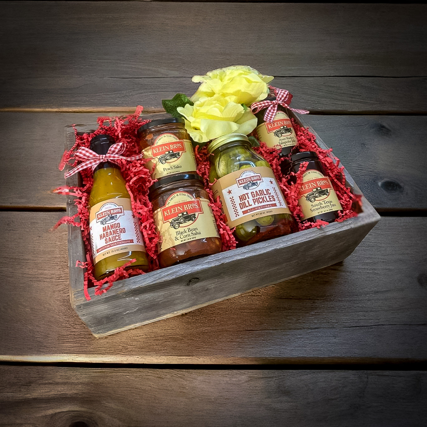 Assorted condiment bottles in a wooden box with decorative flowers on a wooden surface